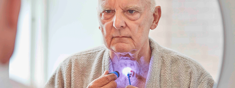 man cleaning voice prosthesis with flashlight in mirror